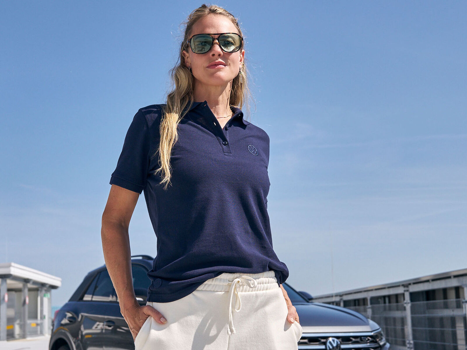 Žena v modrém tričku Volkswagen a vozem Volkswagen za ní