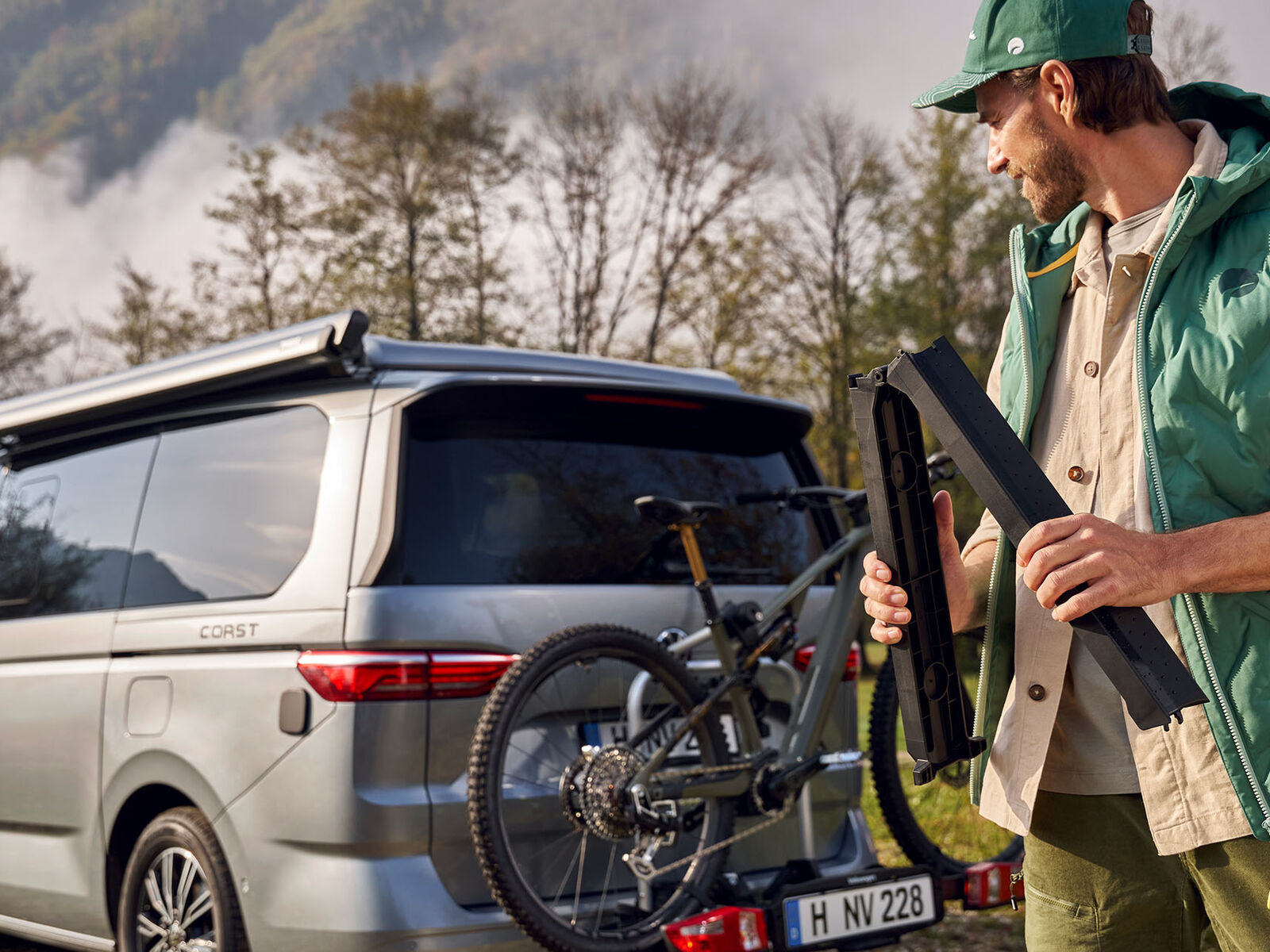 Držák na jízdní kolo na VW T7 a muž v zelené vestě California a zelené kšiltovce California na hlavě