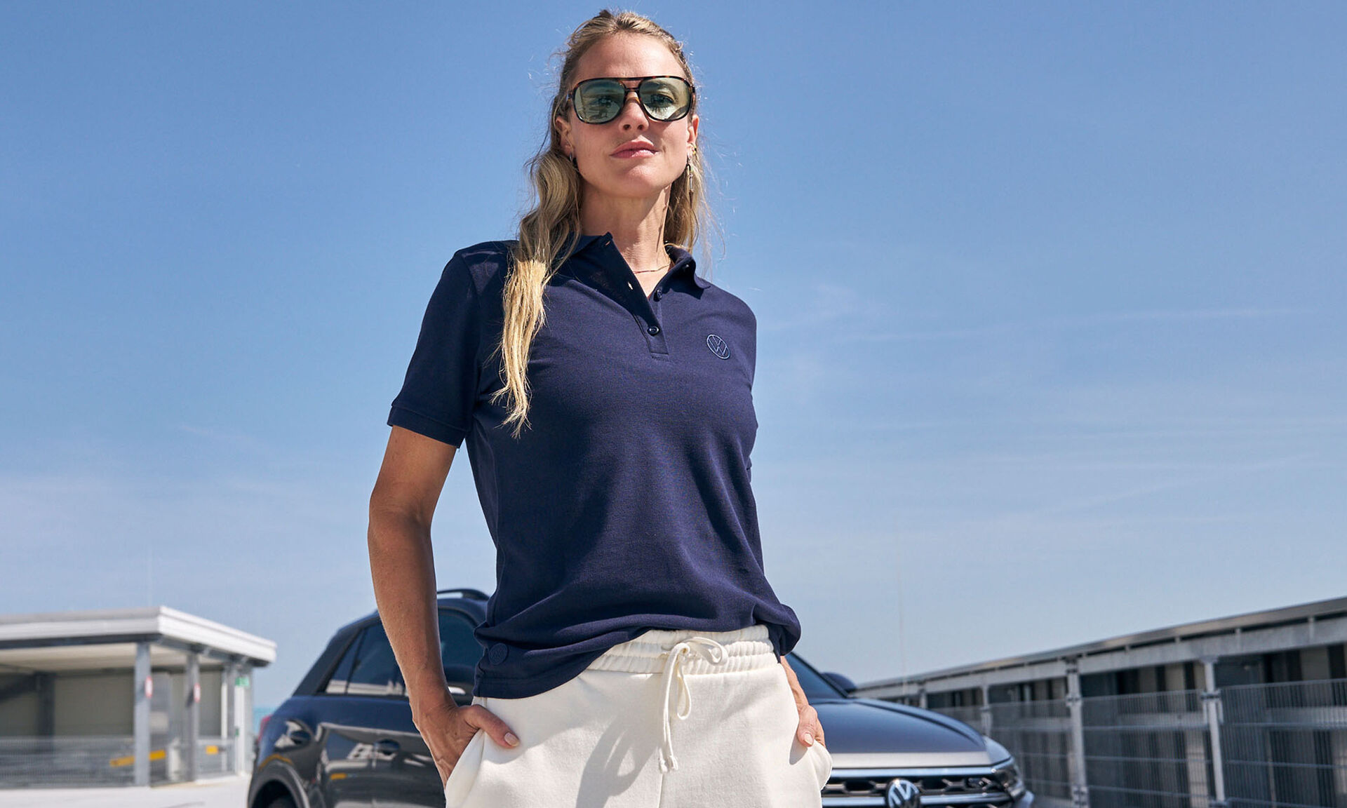 Žena v modrém tričku Volkswagen a vozem Volkswagen za ní