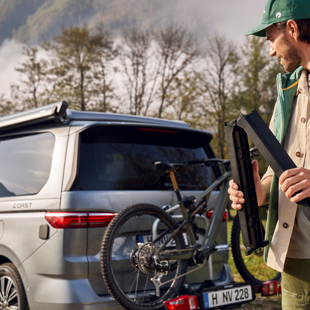 Držák na jízdní kolo na VW T7 a muž v zelené vestě California a zelené kšiltovce California na hlavě