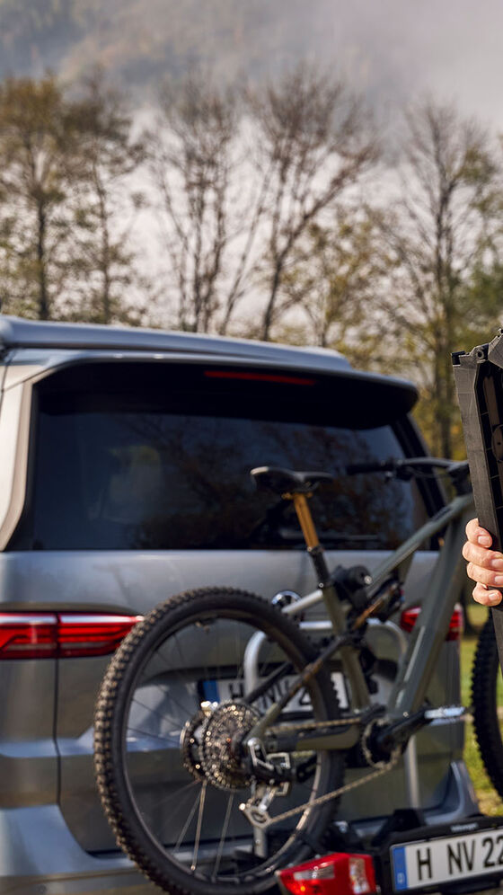 Držák na jízdní kolo na VW T7 a muž v zelené vestě California a zelené kšiltovce California na hlavě